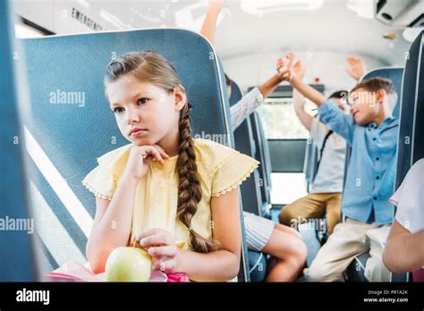 Sad Little Schoolgirl Riding On School Bus While Her Classmates Giving High Five Blurred On