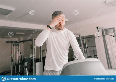 A Tired Man On A Treadmill Wipes Sweat From His Face With His Hand