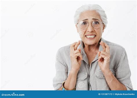 Anxious And Concerned Hopeful Silly Senior Woman In Glasses With White Hair Crossing Fingers For