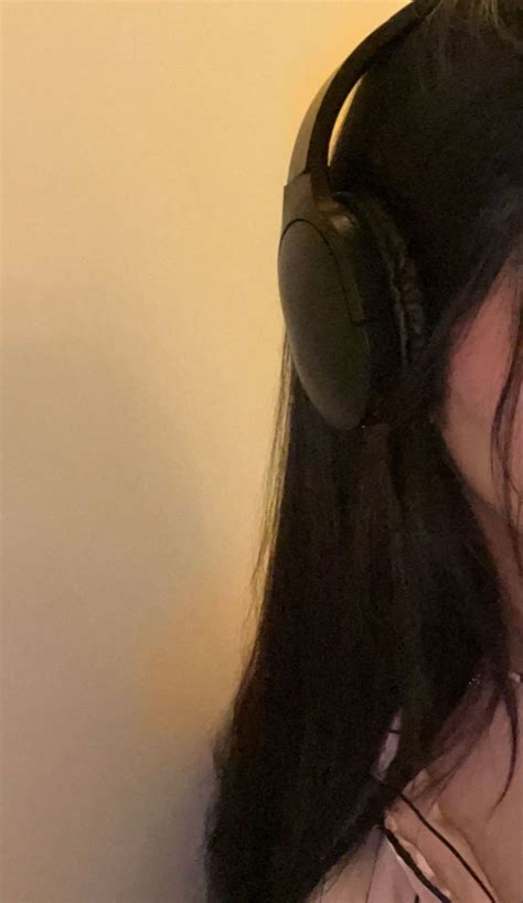 A Woman With Headphones On Her Ears Is Looking At The Phone And Has Long Black Hair