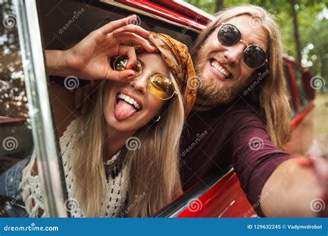photo of caucasian hippie couple smiling and fooling around while driving retro minivan in