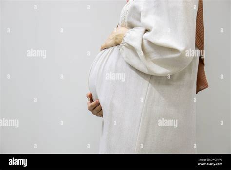 pregnant arabic muslim female on isolated white background touching her tummy showing her body