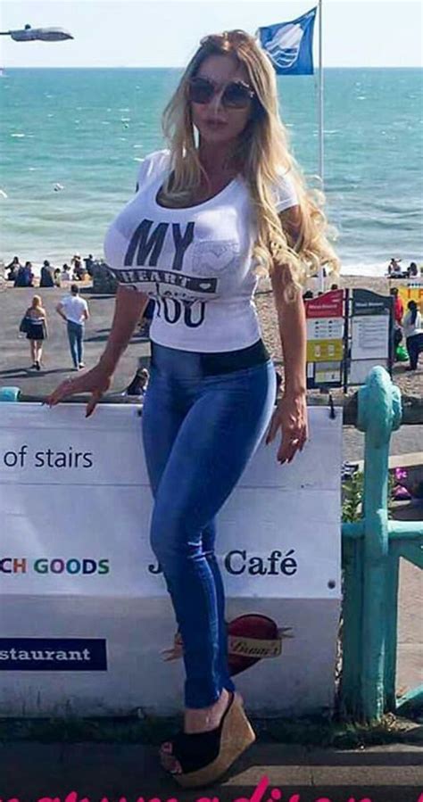 A Woman Standing On Top Of A Sign Next To The Ocean With Her Hands In Her Pockets