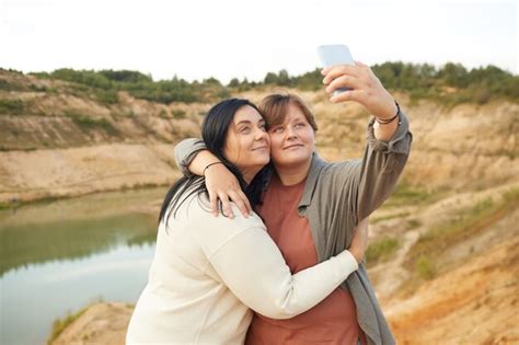 dos jóvenes lesbianas abrazándose y haciendo retrato selfie en teléfono móvil contra el hermoso