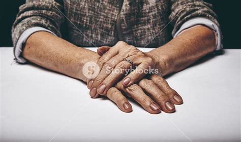 Close Up Studio Shot Of A Senior Womans Hands Resting On Grey Surface