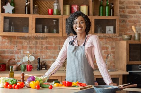Black Woman Cooking Healthy Salad At Kitchen Smiling At Camera Stock