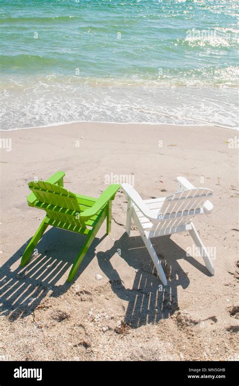 A Pair Of Adirondack Chairs On The Beach Facing The Ocean They Are