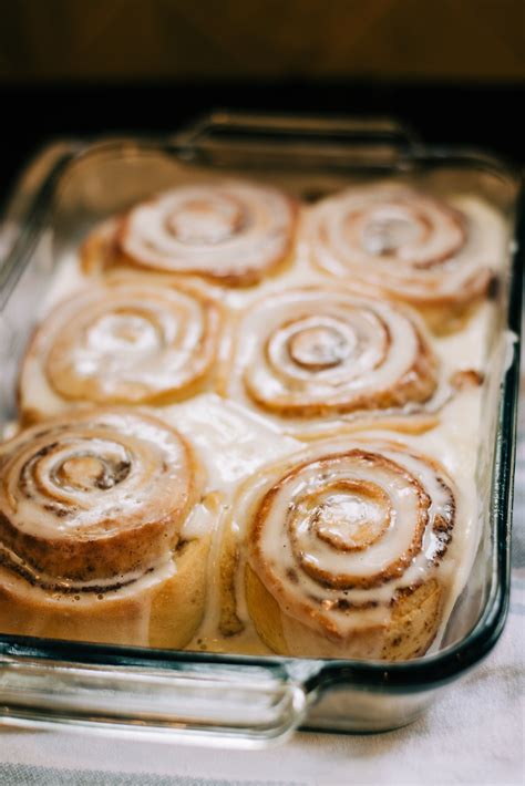 six large cinnamon rolls covered in white icing sit side by side in a glass baking dish on top