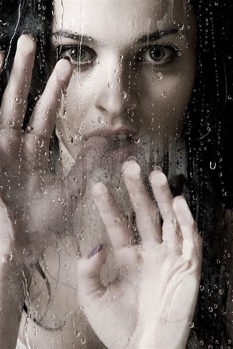 a woman holding her hands to her face while standing in front of a rain covered window