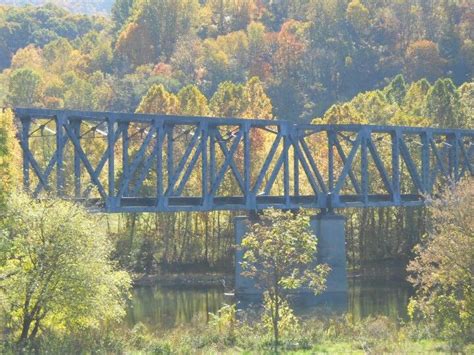 An Old Train Bridge Over A River Surrounded By Trees In The Fall Time