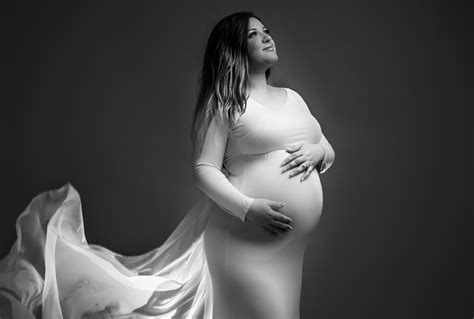 A Maternity Photo Shoot Captures A Pregnant Woman In A White Gown In