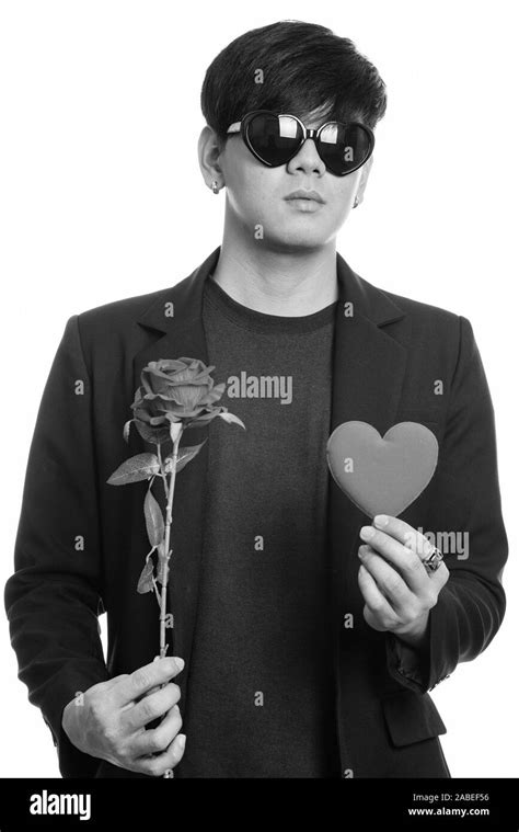 cool handsome asian businessman wearing heart shaped sunglasses while holding red roses and