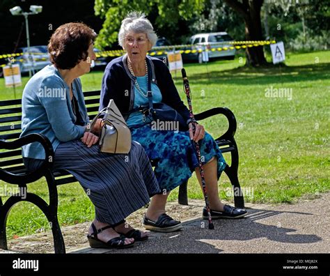 Two Elderly Women Sit On A Bench Talking At Canons Park Harrow London