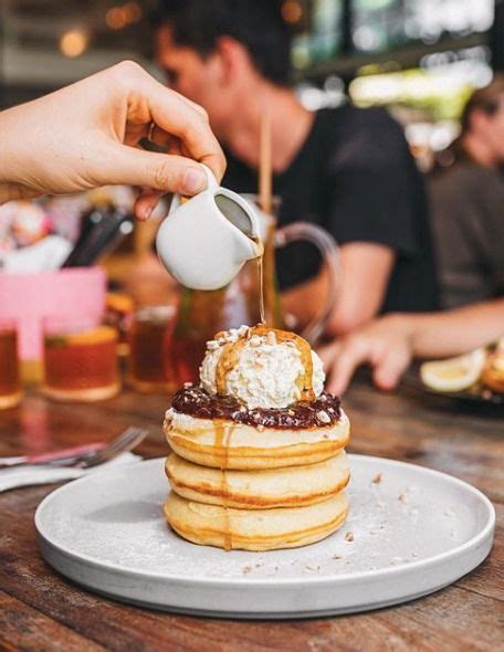 A Person Is Pouring Syrup On Top Of A Stack Of Pancakes At A Table With Other People In The