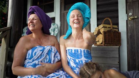three female sauna lovers enjoying fresh air on the porch of a traditional finnish sauna stock