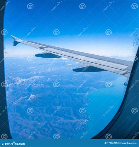 The Wing Of An Airplane Flying Over The Mountains And The Sea Stock