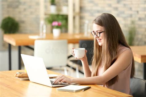 Female Freelancer Drinking Coffee While Working On Laptop In Cafe Stock