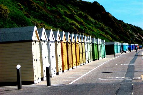A Row Of Beach Huts Sitting On The Side Of A Road Next To A Hill