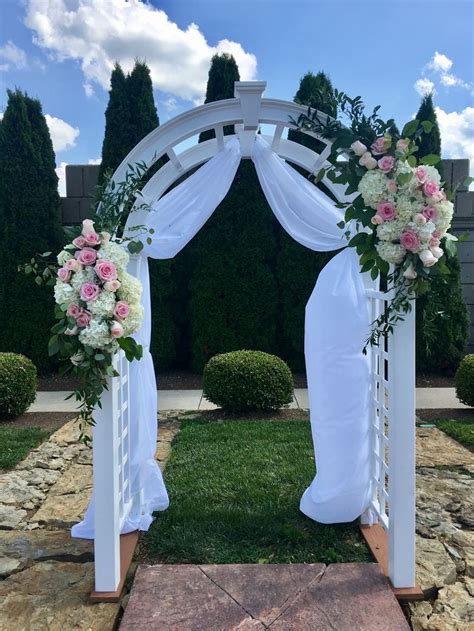 A White Wedding Arch Decorated With Pink And White Flowers
