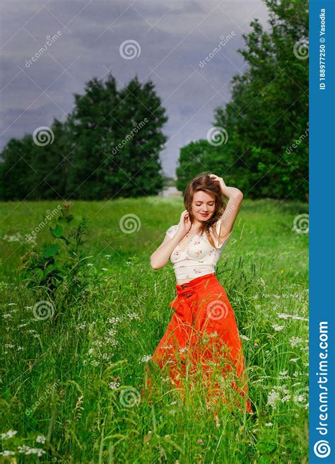 Soft Focus Of Young Brunette Girl In White Top And Red Skirt Standing In Green Meadow Field