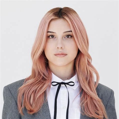 A Woman With Pink Hair Wearing A Gray Suit And Black Bow Tie Looking At The Camera
