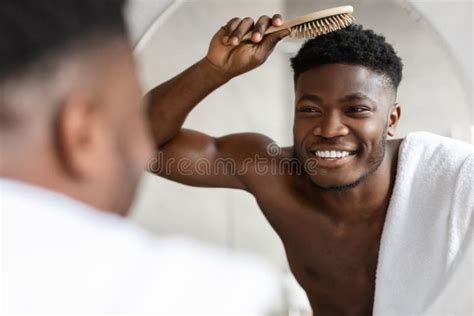 Cheerful Black Guy Brushing Short Hair With Hairbrush In Bathroom Stock