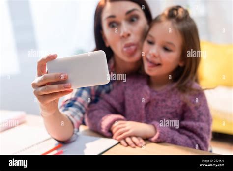 Mother And Daughter With Sticking Out Tongues Taking Selfie At Home On