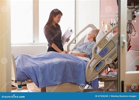 Female Doctor Talks To Senior Female Patient In Hospital Bed Stock