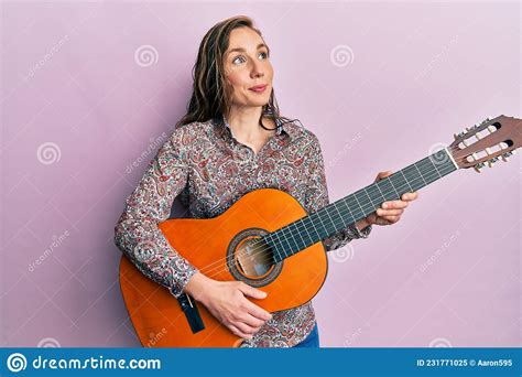 Young Blonde Woman Playing Classical Guitar Smiling Looking To The Side