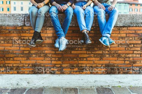 Piernas De Cuatro Adolescentes Sentados En Un Muro De Ladrillos Foto De