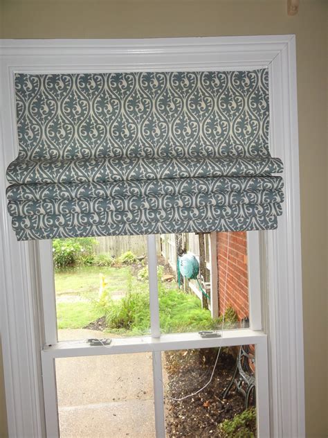 An Open Window With A Blue And White Roman Blind