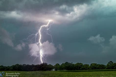 A Lightning Bolt Is Seen In The Sky Over A Grassy Field With Trees On