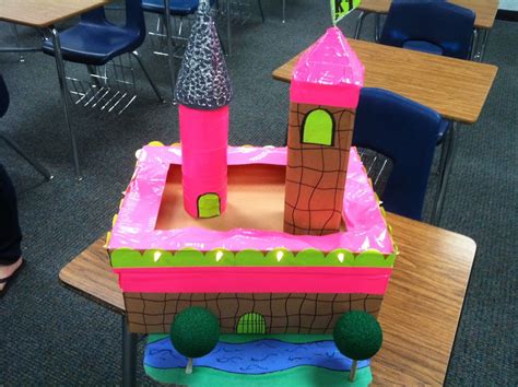 A Cake Shaped Like A Castle On Top Of A Table In A Classroom With Other