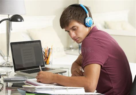 Teenage Boy Studying At Desk In Bedroom Wearing Headphones Stock Image