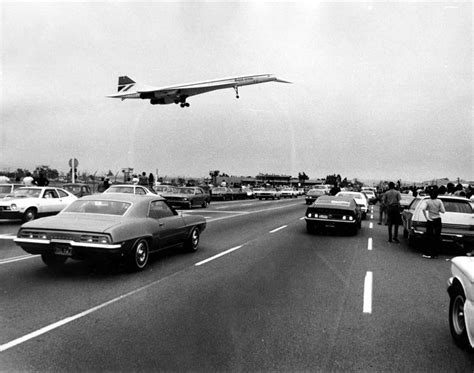 An Airplane Is Flying Over Cars On The Highway As People Watch From The