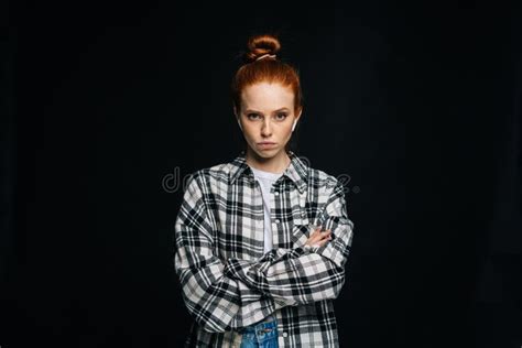Angry Red Haired Young Woman Wearing Wireless Earphones Looking At Camera On Black Background