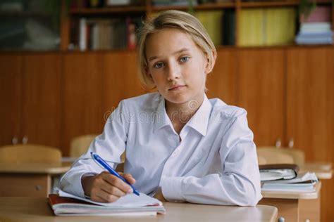 Teenage Boy Writing In Copybook At Desk In Classroom Looking At Camera