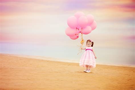 Фото Девочка в розовом платье стоит на песчаном берегу и держит в руке