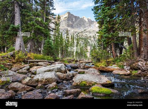 Early Morning Stream Serenity With Boulders And A Rugged Mountain Peak