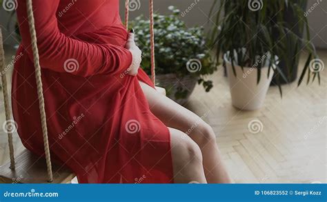 A Charming Pregnant Girl In A Long Red Dress Swinging On The Swing And