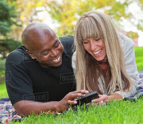 Interracial Couple Looking At Text Messages In The Park Edmonton