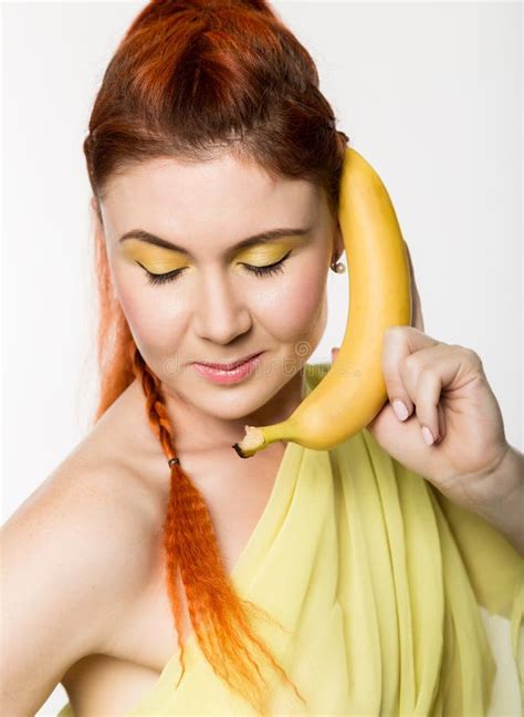 Young Redhead Woman Holding Banana Near Her Face Like Smartphone On A