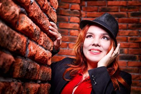 Beautiful Young Woman With Redhair And Black Hat Being Near Red Brick