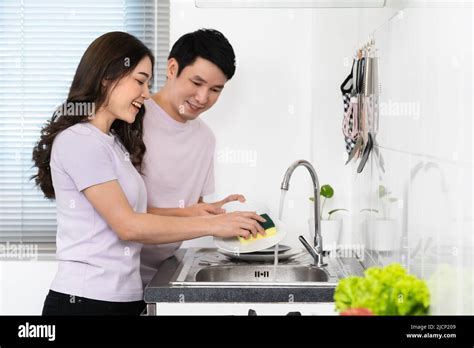 Happy Young Couple Washing Dishes Together In The Sink In The Kitchen