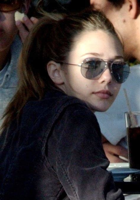 A Woman Wearing Sunglasses Sitting At A Table With A Beverage In Front