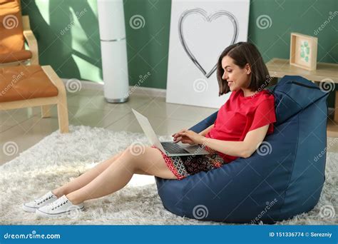 Young Woman With Laptop Sitting On Beanbag Chair At Home Stock Photo