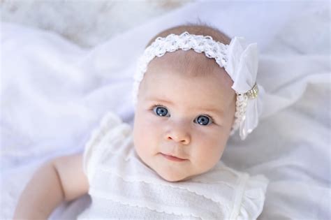 카메라를 보고 흰색 배경에 그녀의 등에 누워 흰 옷에 파란 눈을 가진 귀여운 아기 소녀 프리미엄 사진