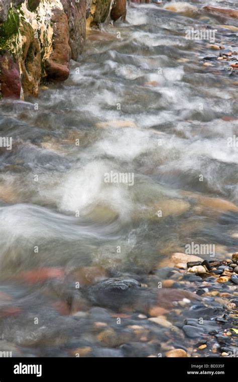 Photograph Of Fast Moving Water Flowing Against A Wall Over Rocks And