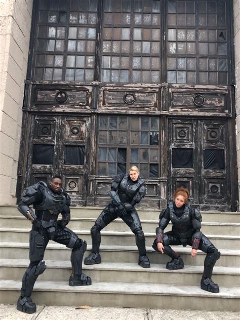 Four People Dressed In Black Sit On The Steps Outside An Old Building And Pose For A Photo