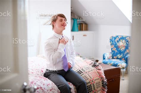 Young Downs Syndrome Man Sitting On Bed Getting Dressed For Work Stock